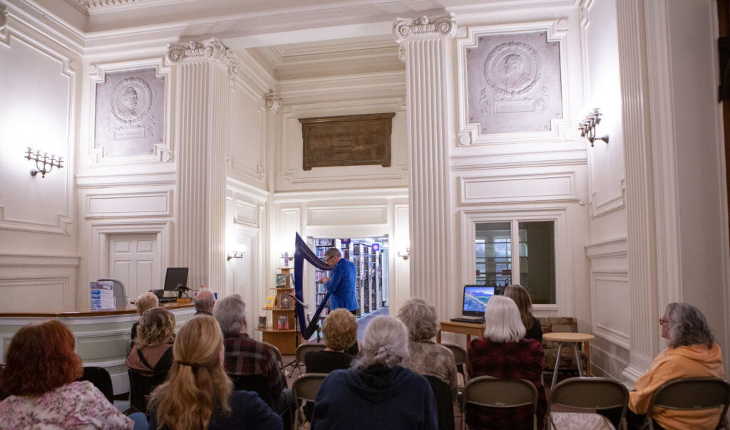 Music in the Stacks -- concert in the Historic Main Lobby of Seymour Library with harpist playing in front of a crowd.